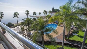 A pool area with palm trees, a view of the sea, and a building in the background.