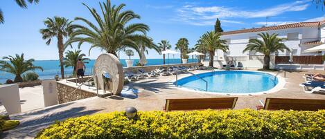 A pool area with lounge chairs and palm trees, overlooking the sea.