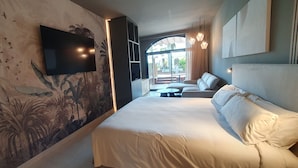 A modern hotel room with a large bed, a flat-screen TV mounted on the wall, and a view of the outdoor area through a glass door. - Miami Mar - Boutique Hotel & Restaurant (Sant Carles de la Rapita)