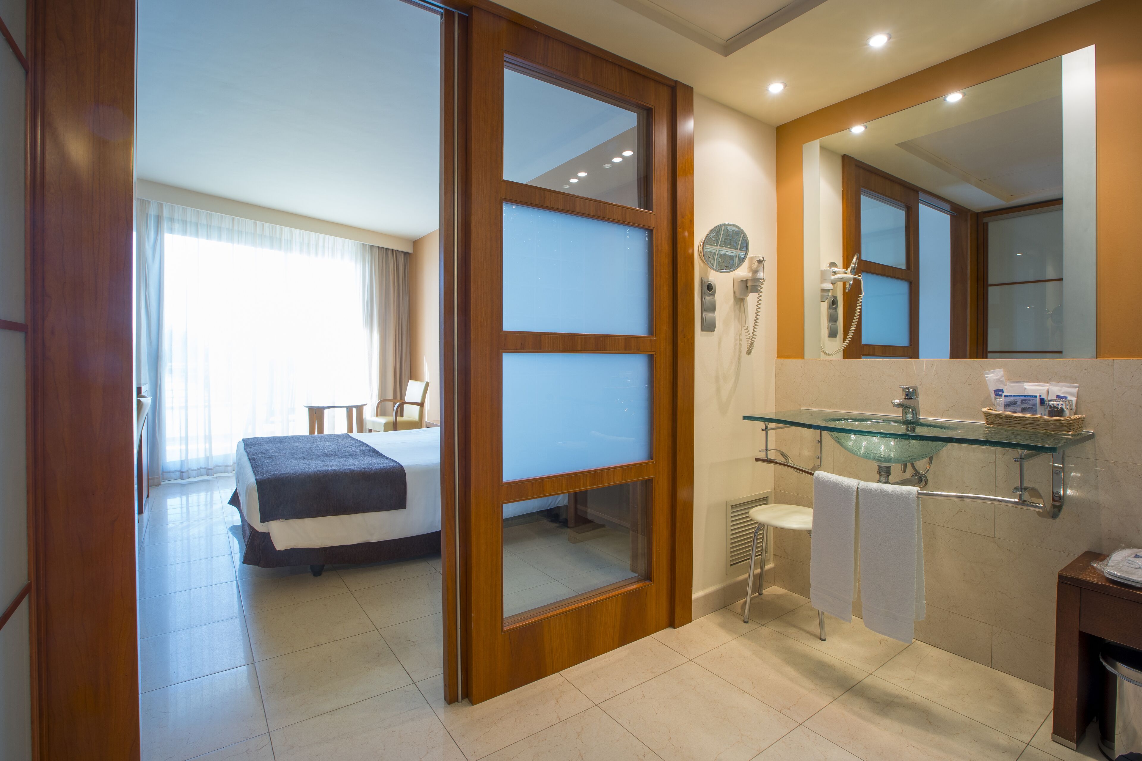 Een hotelkamer met een bed, een badkamer met glazen wanden en een grote spiegel.
