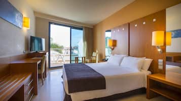 A hotel room with a large bed, a desk, a chair, a TV, and a balcony with a view.