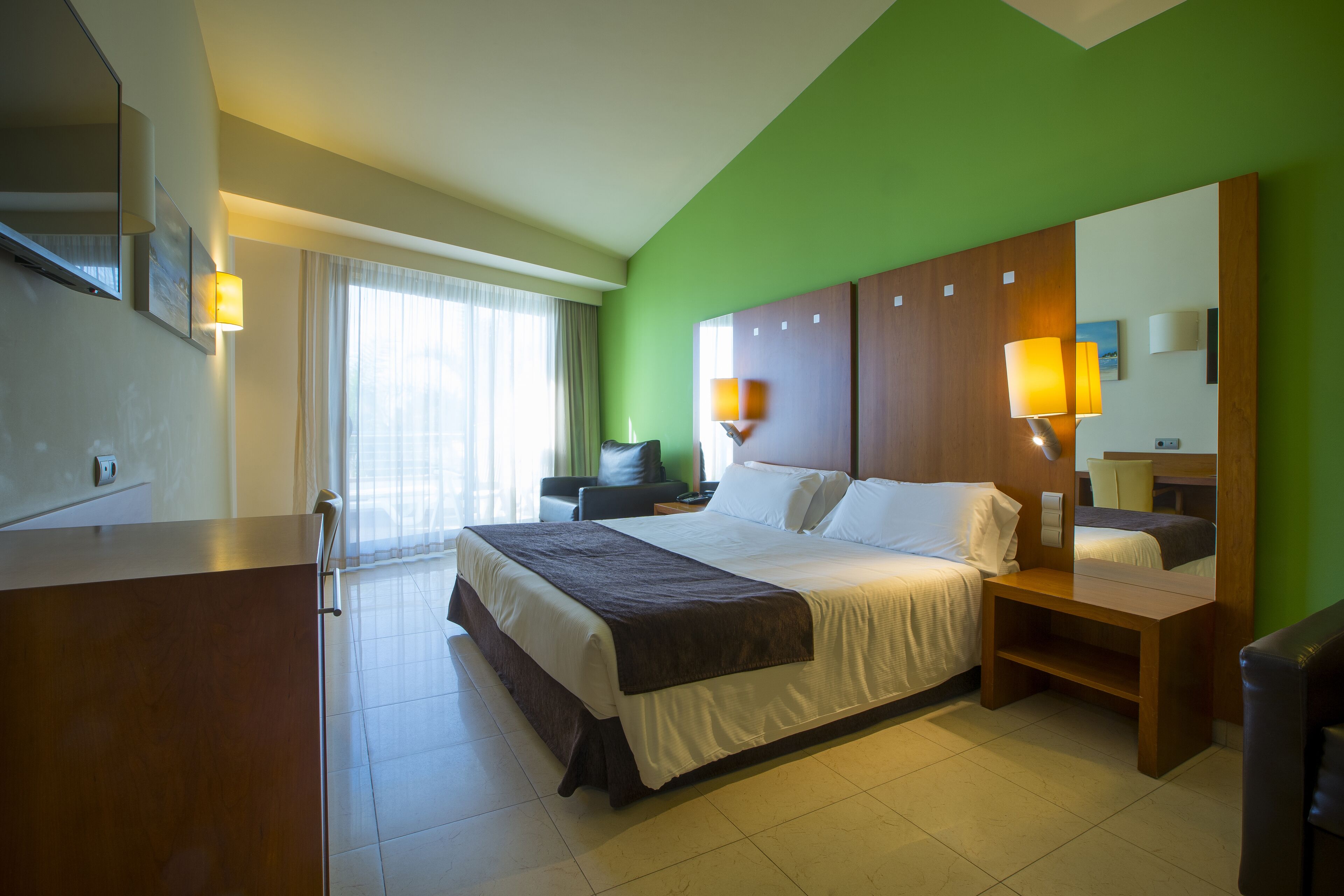 A hotel room with a large bed, a desk, a chair, and a mirror.