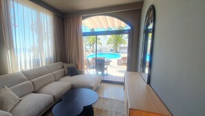 A modern living room with a beige sofa, a round coffee table, and a view of an outdoor pool area through large glass doors. - Miami Mar - Boutique Hotel & Restaurant (Sant Carles de la Rapita)