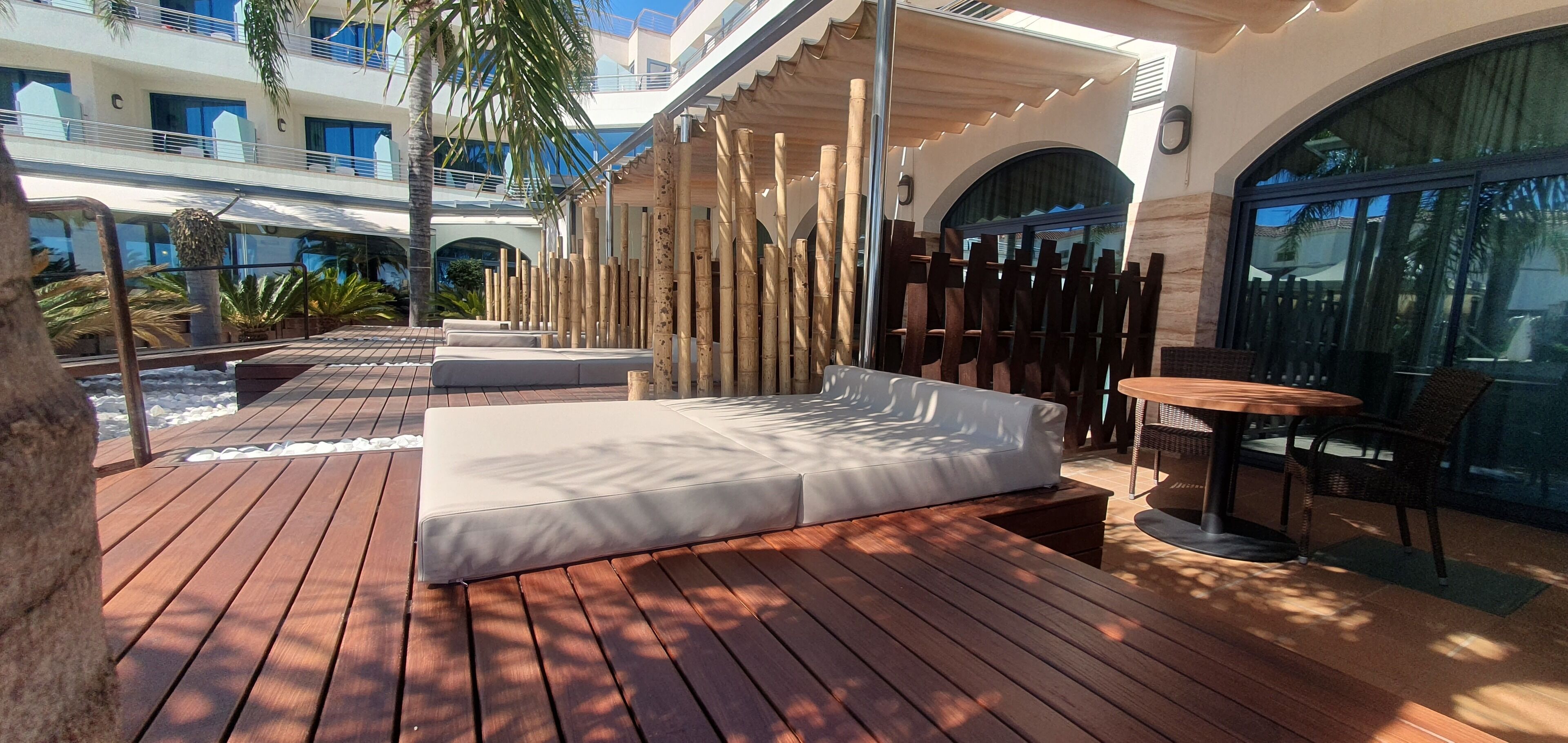 A wooden deck with a sofa and a table, surrounded by bamboo pillars, overlooking a pool area.