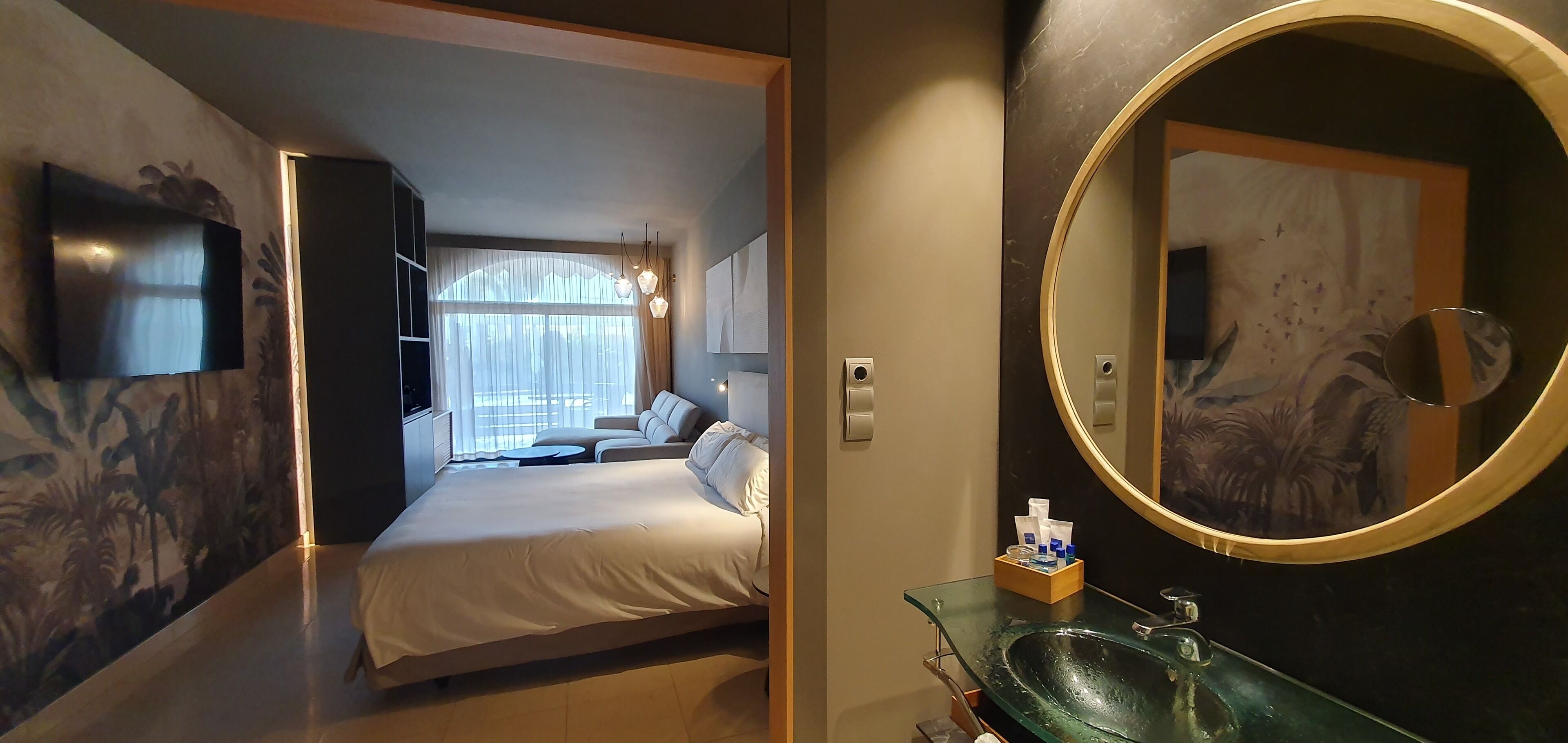 Une chambre d’hôtel équipée d’un lit, d’un lavabo en verre, d’un grand miroir et d’un téléviseur fixé au mur.