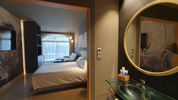 Une chambre d’hôtel équipée d’un lit, d’un lavabo en verre, d’un grand miroir et d’un téléviseur fixé au mur.