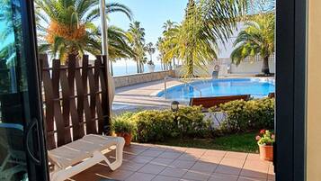 A glass door leading to a patio with a pool, palm trees, and a wooden fence.