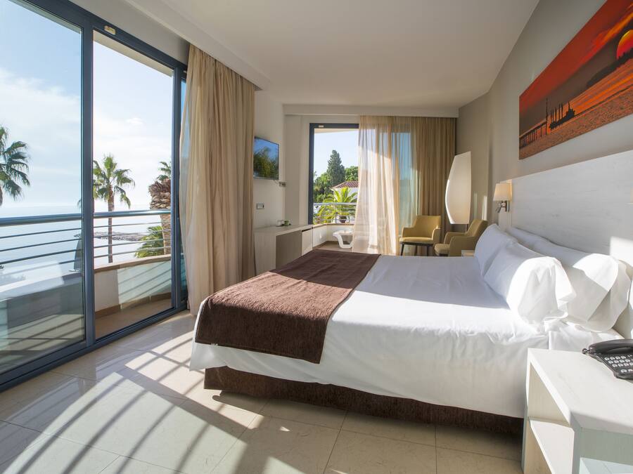 A hotel room with a large bed, a desk, a chair, a phone, and a view of the ocean.