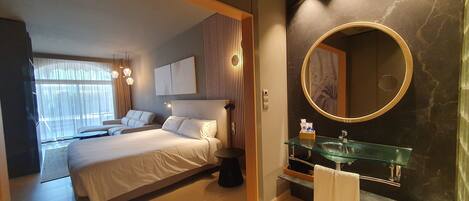 A modern bedroom with a large bed, a glass bathroom vanity, and a large mirror.