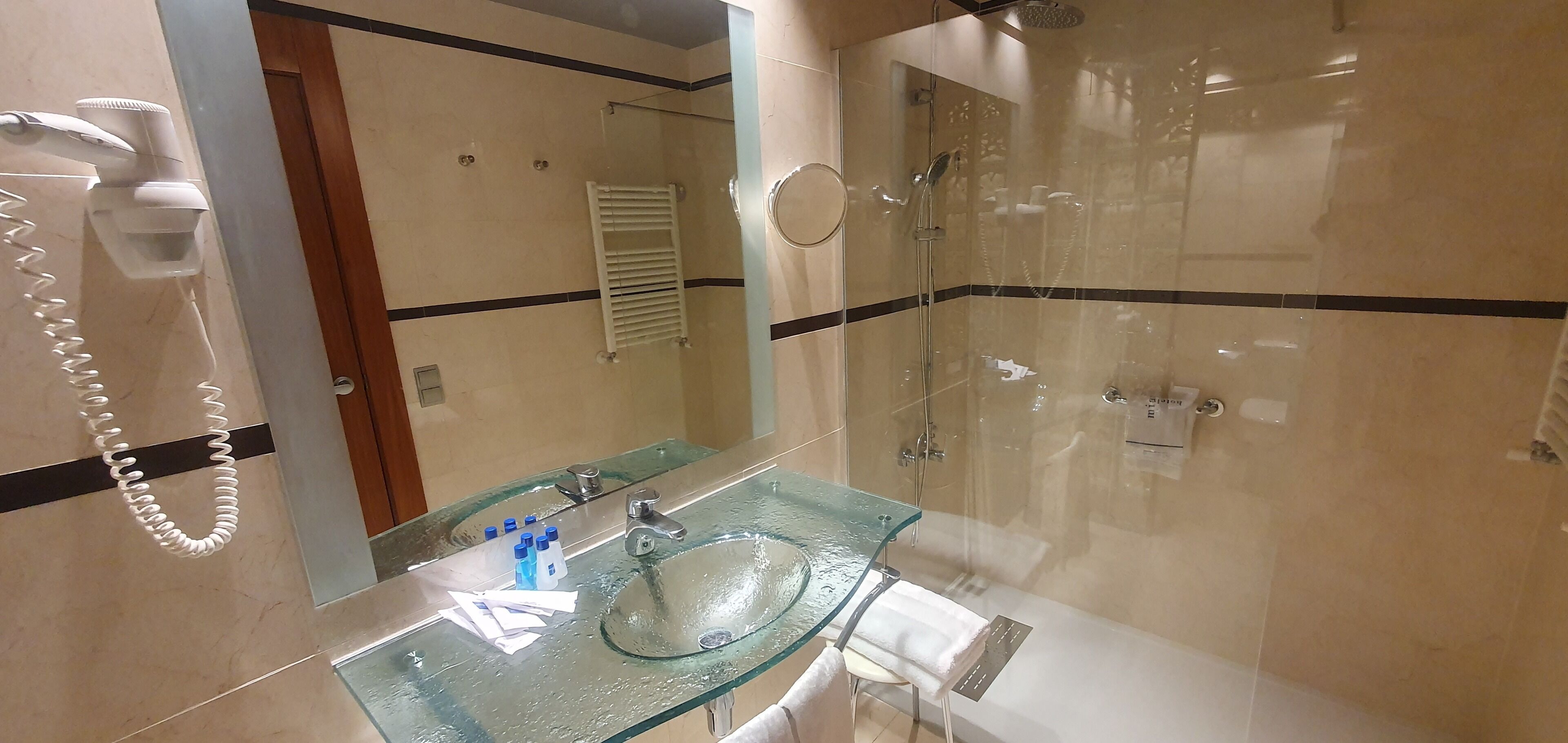 A modern bathroom with a glass sink, a handheld hair dryer, and a walk-in shower.