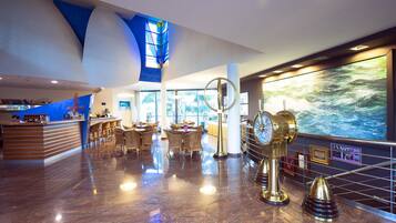 A modern hotel lobby with a reception desk, seating area, and a large window with a view of the outdoors.