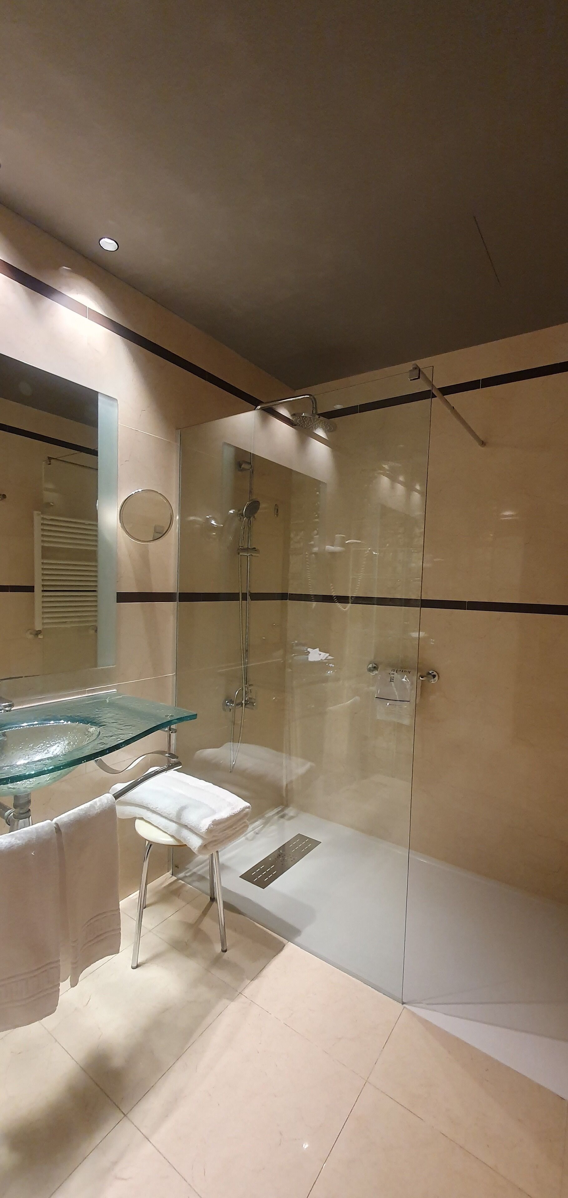 Une salle de bain moderne avec une douche à parois de verre, un lavabo en verre et une serviette blanche posée sur un tabouret.