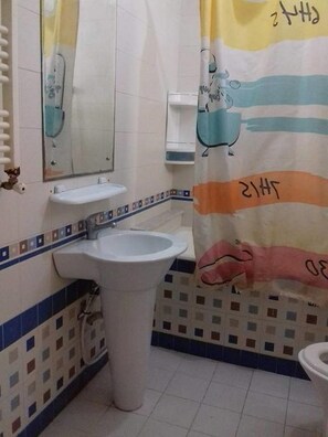 A bathroom with a white sink, a mirror, and a toilet. There is a colorful shower curtain with a cartoon character and the text "CHRIS". - Benzineb Immo Menzeh (Ariana)