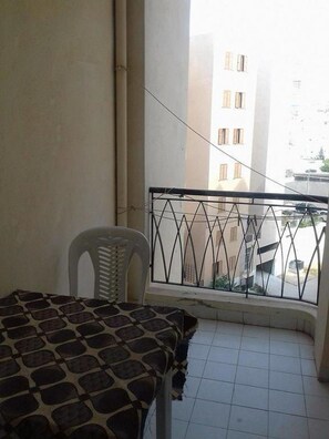 A balcony with a patterned table and a white chair, a metal railing, and a view of buildings in the background. - Benzineb Immo Menzeh (Ariana)