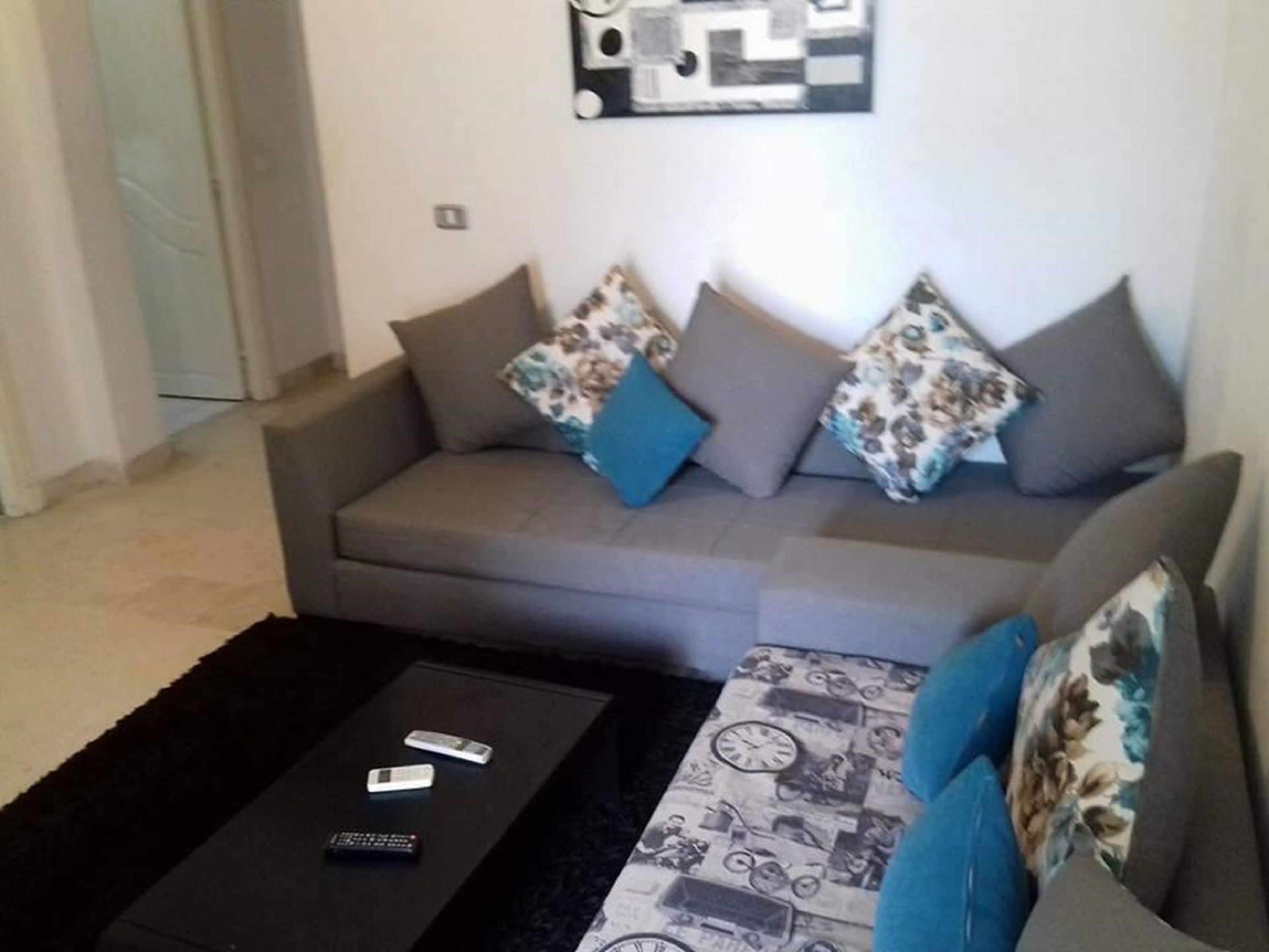 A living room with a grey sofa, two blue cushions, and a black coffee table with remote controls.