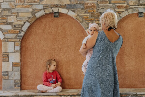 A stone wall with a circular window and a child sitting on the ground.