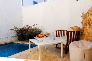 Un pequeño espacio al aire libre con piscina, una mesa con bebidas y plantas en macetas.