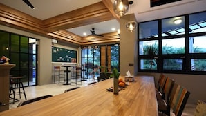 Un espace repas moderne avec une longue table en bois, de nombreuses chaises et un coin bar équipé de tabourets.