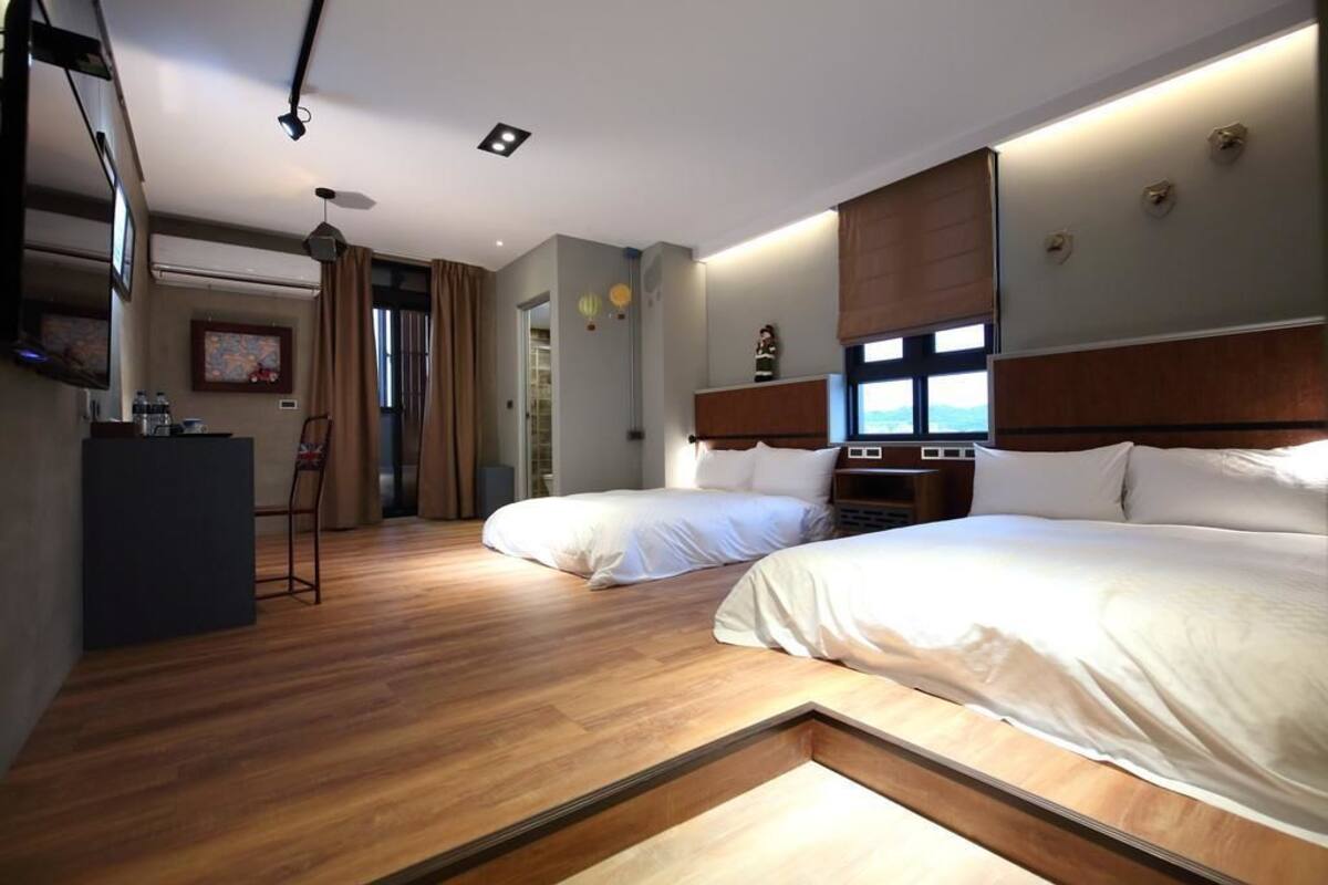 Habitación de hotel con dos camas, un escritorio y vistas al exterior.