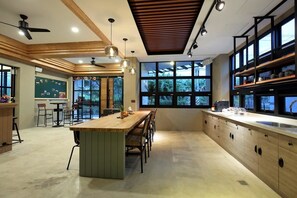 A modern kitchen with a central island, wooden cabinets, and a large window providing a view of greenery. - Midori Hostel (Hualien City)