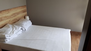 Una cama bien hecha con sábanas y almohadas blancas, un cabecero de madera y una pared lisa.