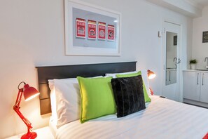 A hotel room with a bed, pillows, a framed picture, a nightstand, and a red lamp. - Idyllic City Studio Air-Con & Wifi (Auckland)