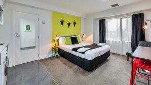 Una habitación de hotel moderna con una cama, lámparas de noche, un escritorio y una ventana con cortinas.