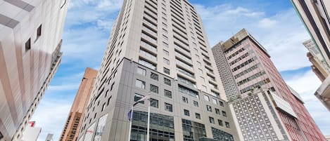 A high-rise building with a modern architectural design, featuring a prominent glass facade and multiple balconies.