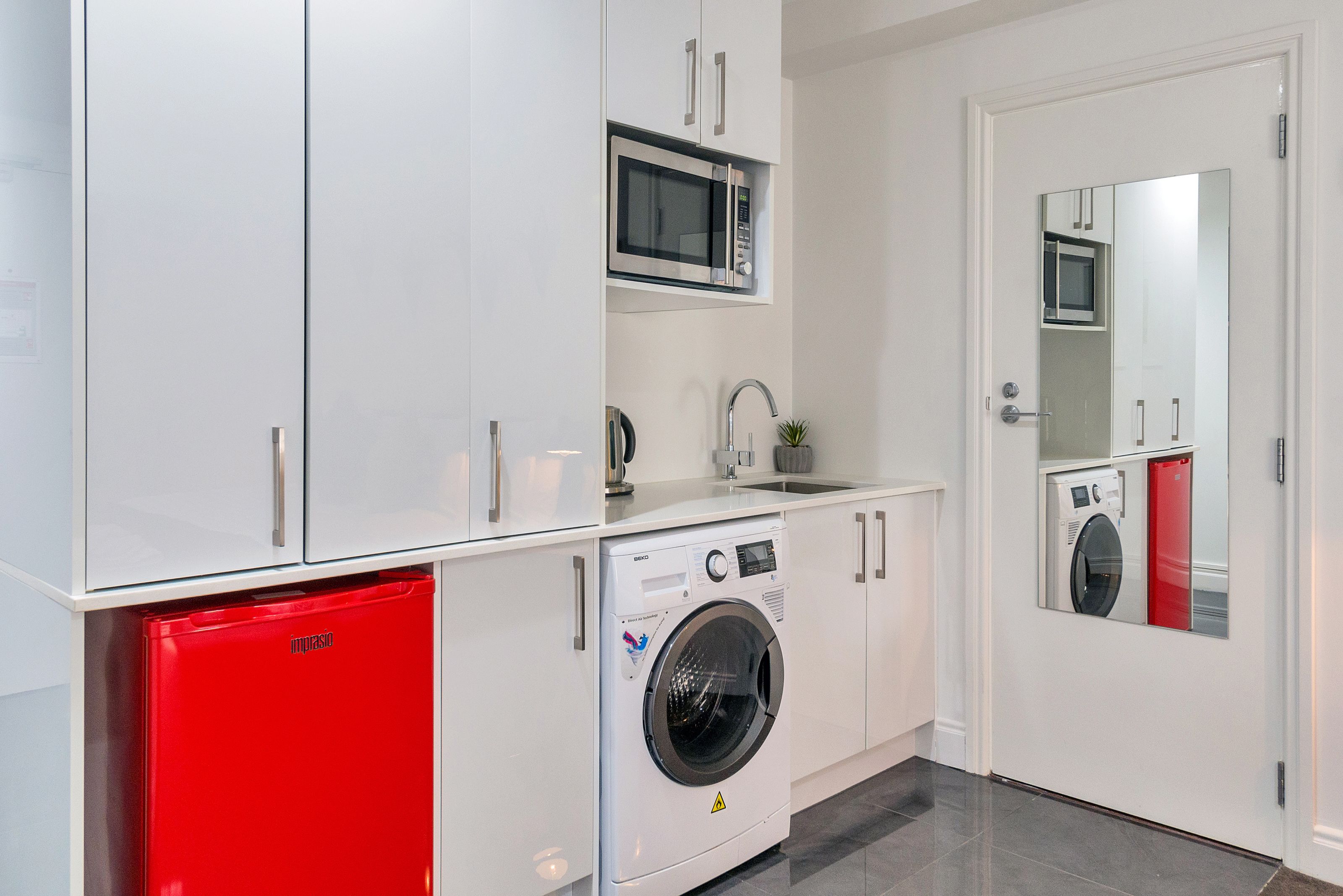 Een kleine keuken met een ingebouwde magnetron, een wasmachine en een rode mini-koelkast.