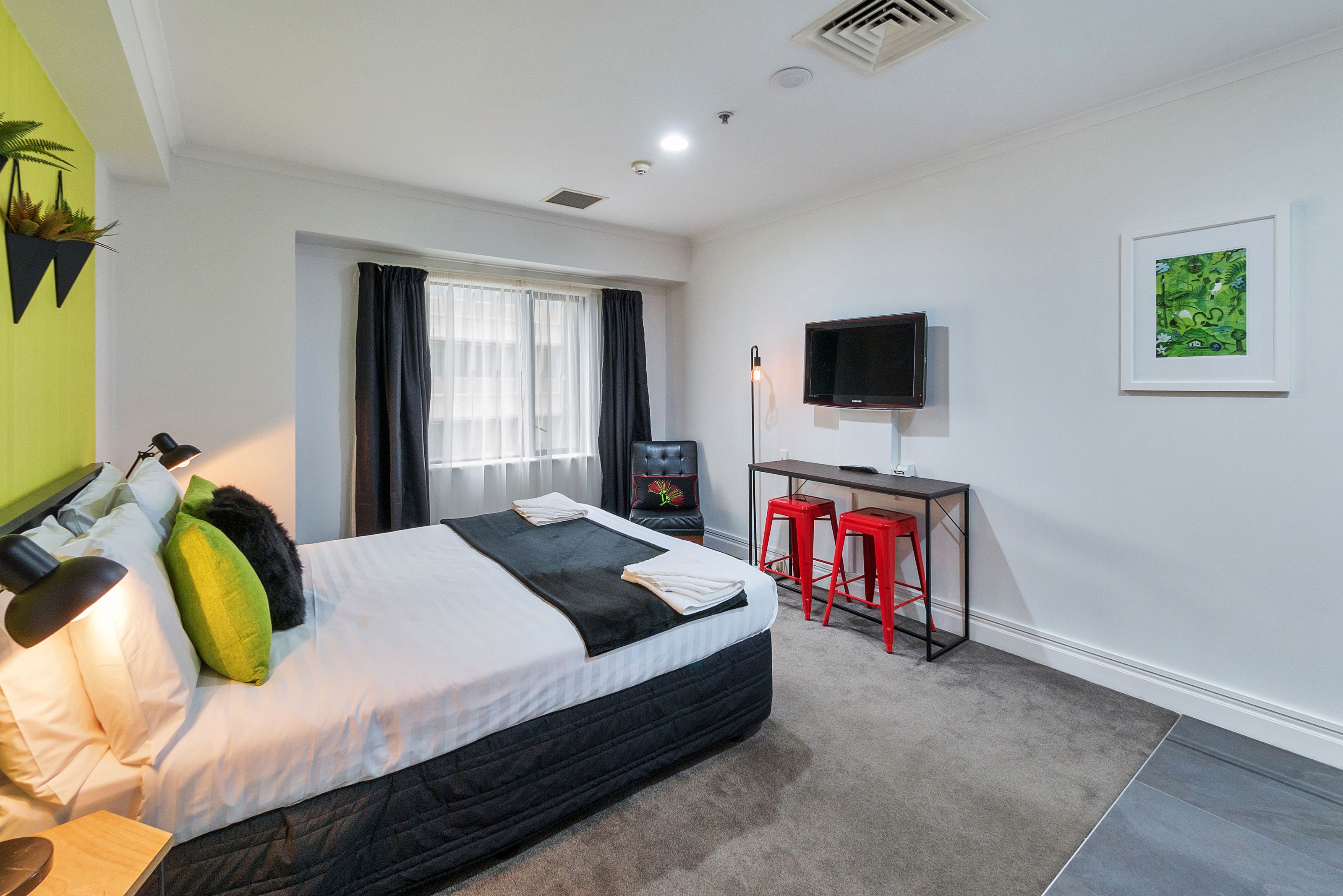 A modern hotel room with a large bed, a desk with a chair, a TV, and a window with curtains.