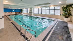Una piscina interior con agua cristalina, paredes de azulejos y una zona de estar con sillones.