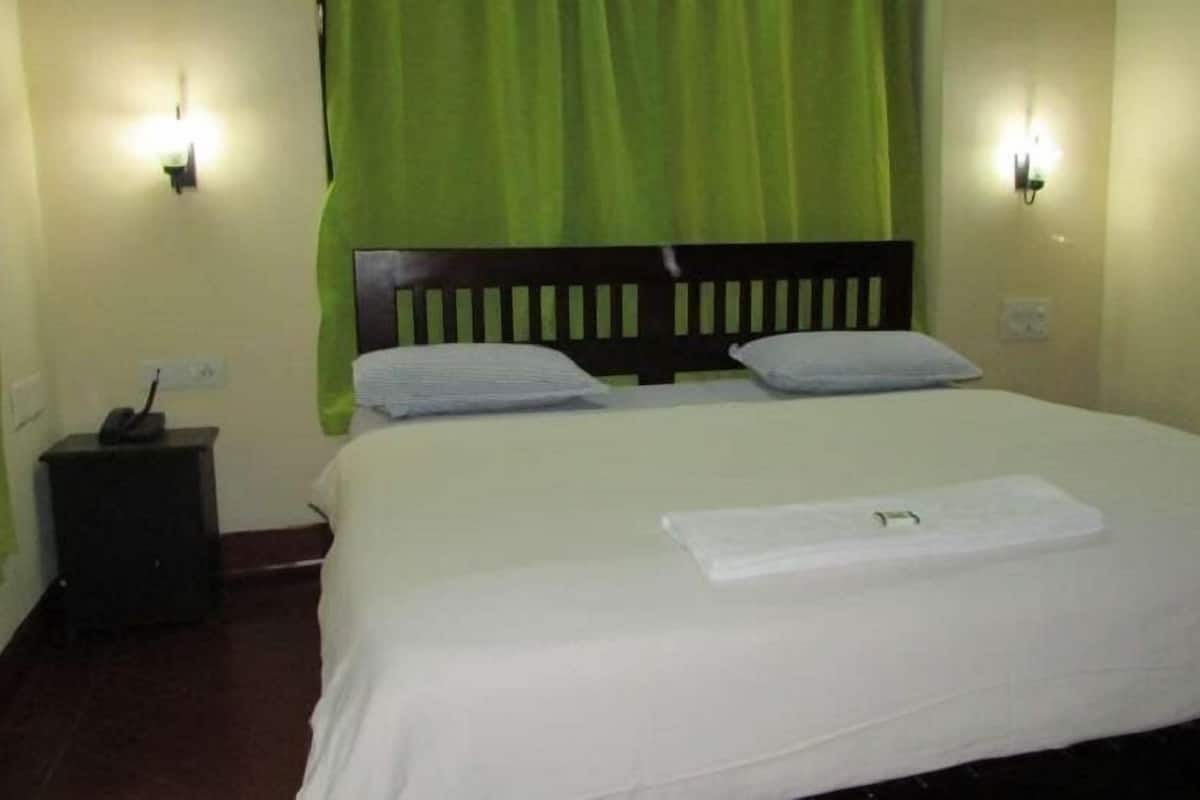Une chambre d’hôtel avec un lit, des rideaux verts, une table de chevet et une lampe fixée au mur.