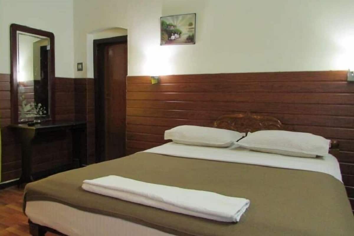 Une chambre d’hôtel avec un lit, une tête de lit en bois, une table de chevet, un miroir et un rideau vert.