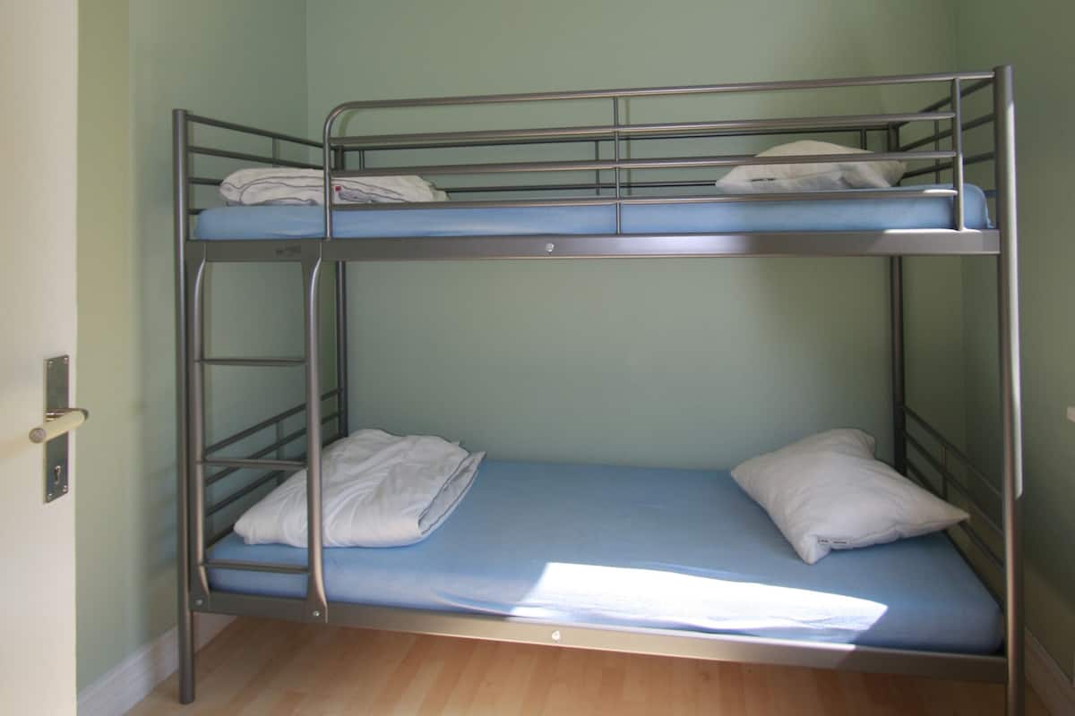 Dormitorio con literas, suelo de madera y lámpara de techo blanca.