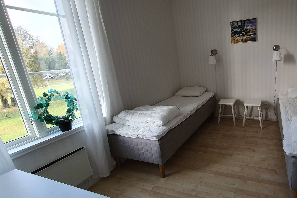 Una habitación pequeña y ordenada con dos camas individuales, una mesita y una ventana con vista a un área verde.