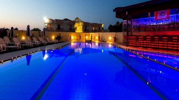 A swimming pool with lounge chairs and a bar area with a Budweiser sign. - Aris Apartments (Malia)