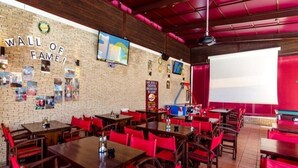A restaurant with a brick wall, red chairs, and tables. - Aris Apartments (Malia)