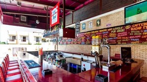 A bar area with a red counter, stools, and a menu board displaying various food and drink options. - Aris Apartments (Malia)