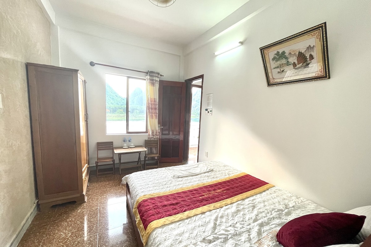 Ein Hotelzimmer mit Bett, Schreibtisch mit Stühlen, Fenster mit Blick ins Grüne und einem Bild an der Wand.