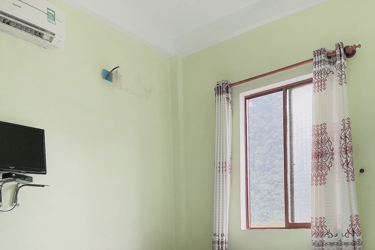 Ein Zimmer mit zwei Betten, einem Fernseher, einer Klimaanlage und einem Fenster mit gemusterten Vorhängen.