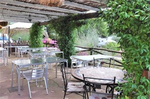 An outdoor patio area with metal tables and chairs, surrounded by greenery and a thatched roof structure. - Villa Agnese (Badesi)