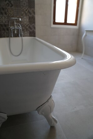 A white clawfoot bathtub in a bathroom with a patterned wall and a window with wooden frames. - Palais de Luppé (Arles)