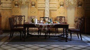 A dining table set with various dishes and a pitcher, surrounded by chairs in a room with ornate wall decorations and a checkered floor. - Palais de Luppé (Arles)