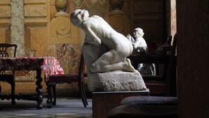 A room with a marble floor, a statue of a seated figure, a wooden bench, and a wall with a mural. - Palais de Luppé (Arles)