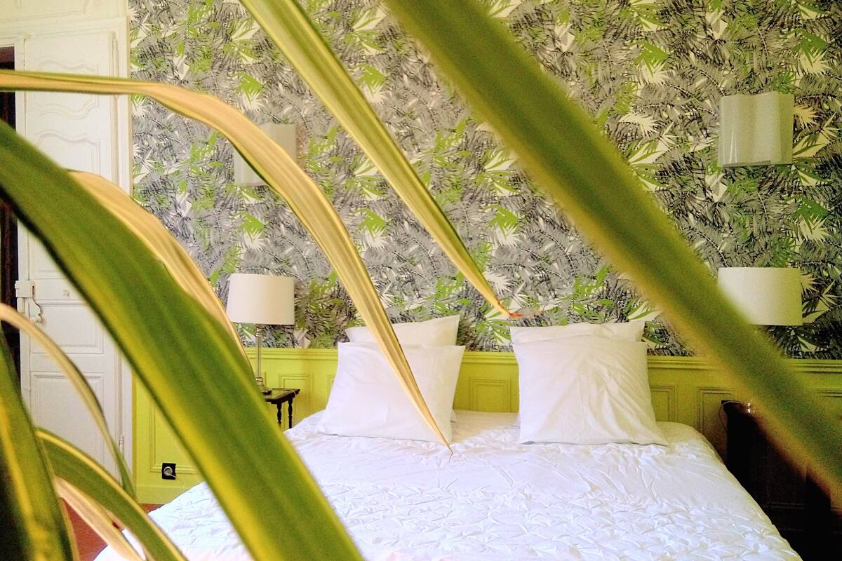 A bed with white linens, a green headboard, and a wall with a leafy wallpaper pattern.