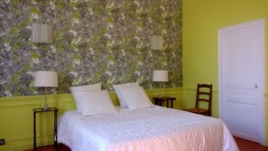 A bedroom with a bed, two bedside lamps, a chair, and a door. - Palais de Luppé (Arles)