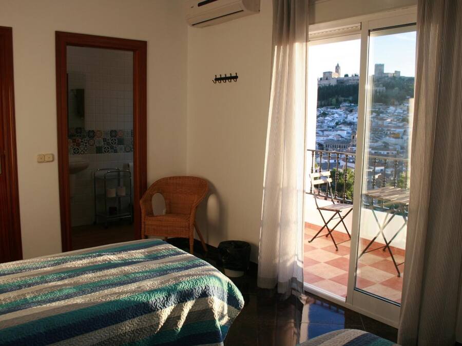 Ein Hotelzimmer mit Bett, Stuhl, einem Balkon mit Schachbrettmuster und Blick auf die Stadt.