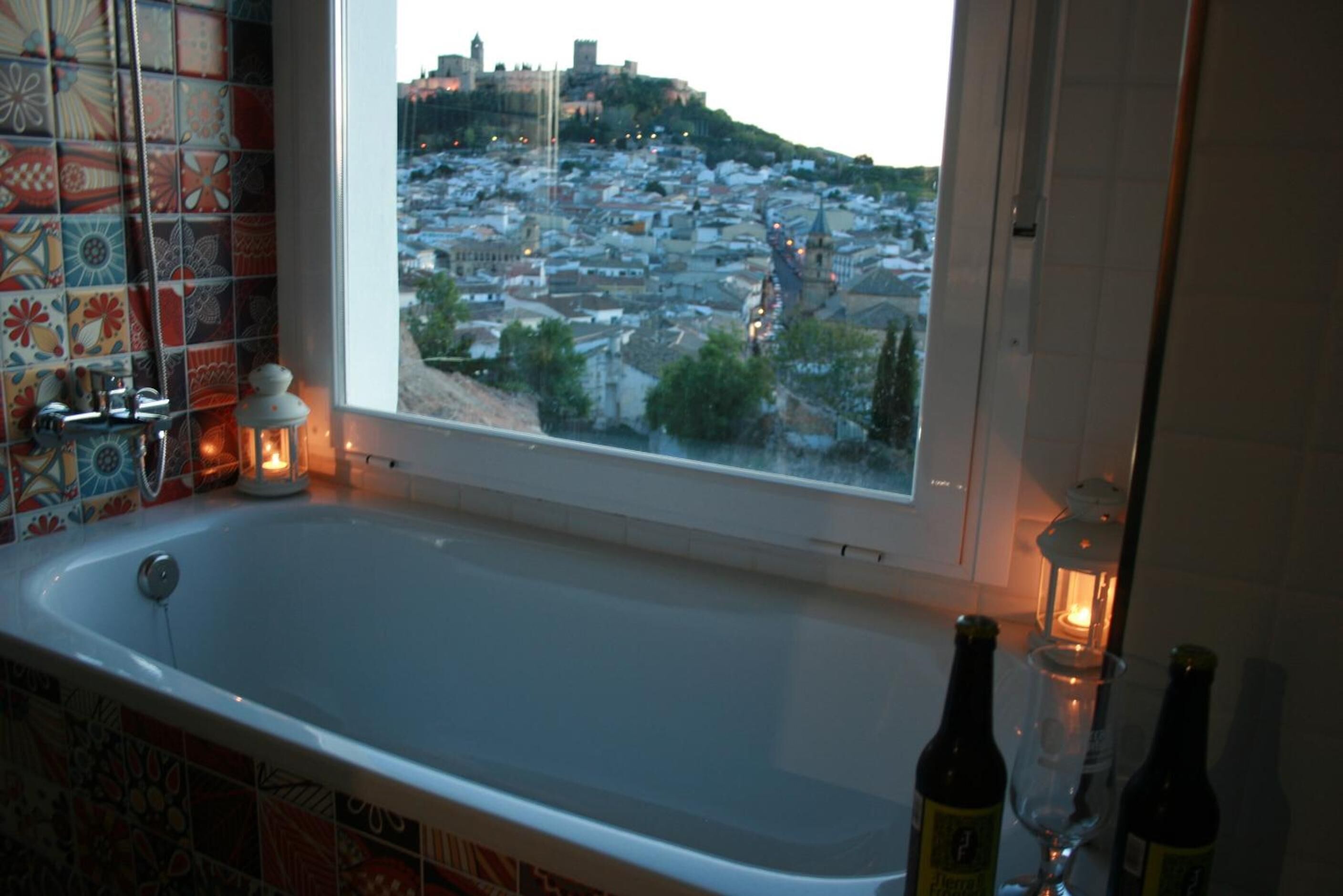 A bathroom with a bathtub, a window with a view of a cityscape, and two bottles on the counter.