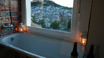 Une salle de bain avec une baignoire, une fenêtre donnant sur un paysage urbain et deux bouteilles posées sur le comptoir.