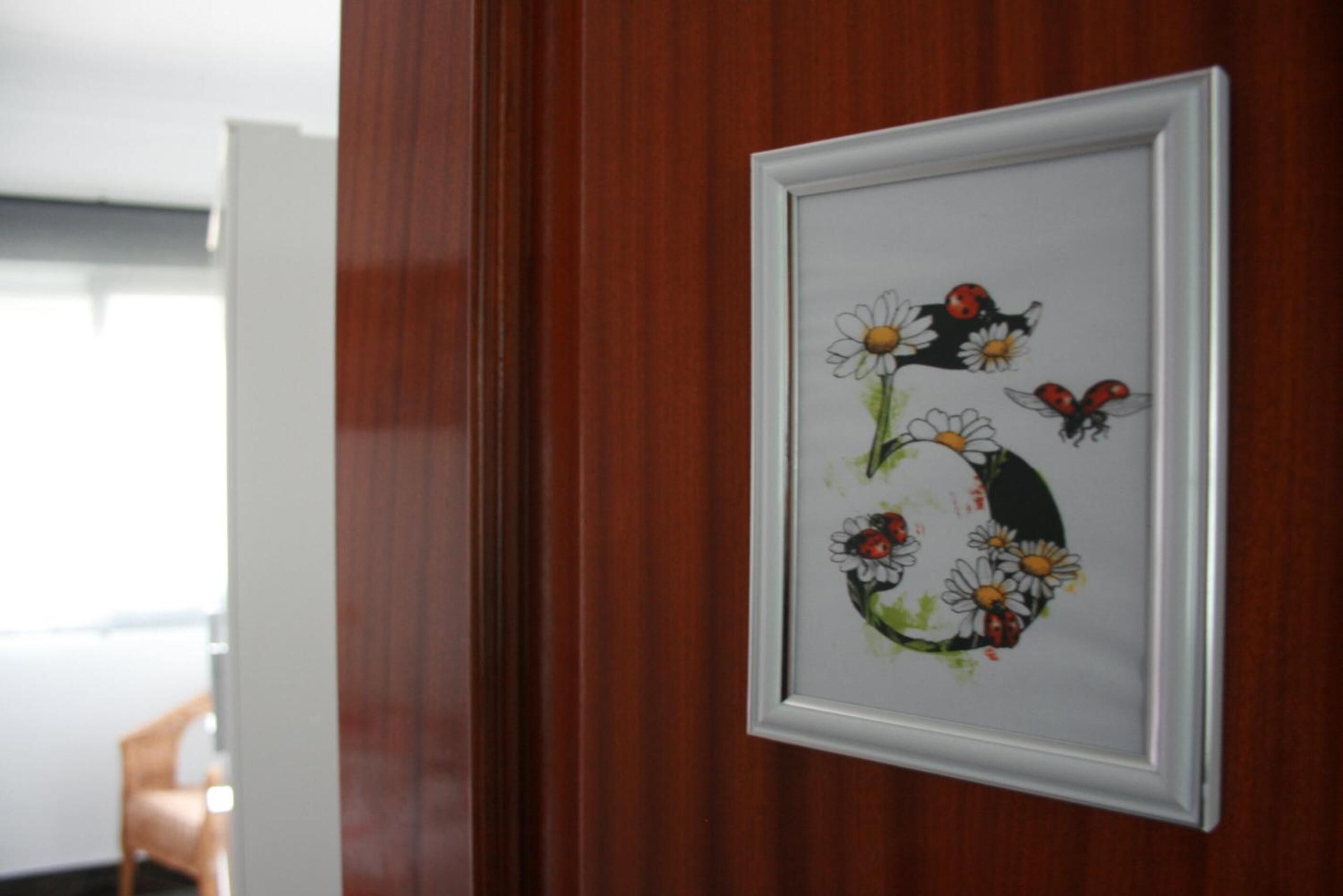 Une œuvre d’art encadrée représentant des fleurs et des coccinelles, accrochée à un mur en bois.